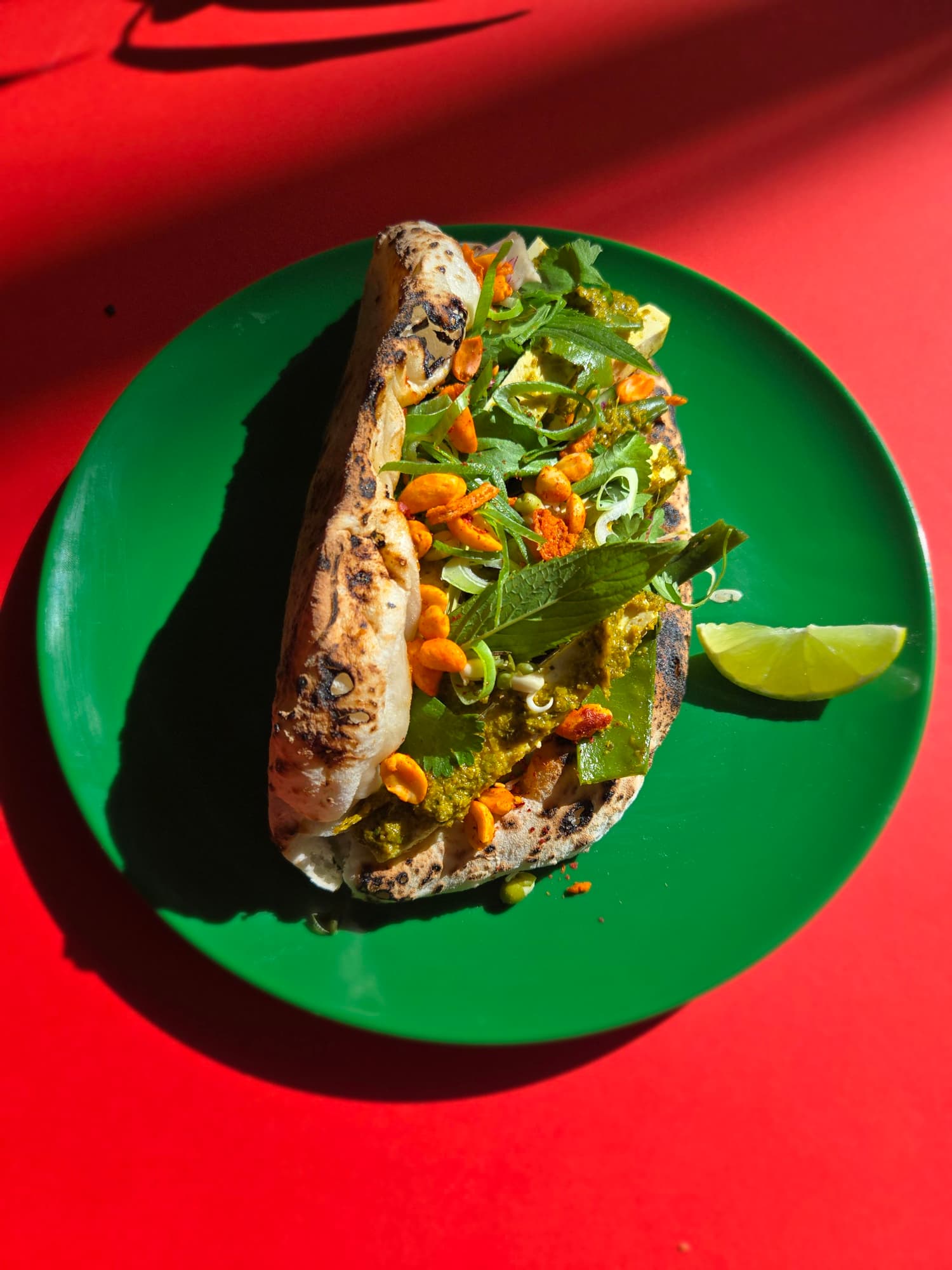 A Thai High ozzo on a green plate against a red backdrop — the 72-hour fermented bread visible at the edges