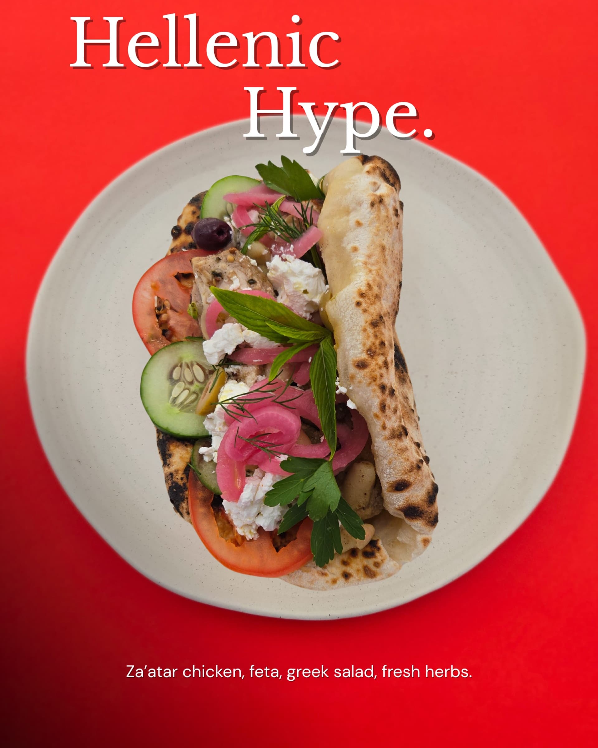 Hellenic Hype ozzo on a white plate against a red backdrop — za'atar chicken, feta, Greek salad, fresh herbs