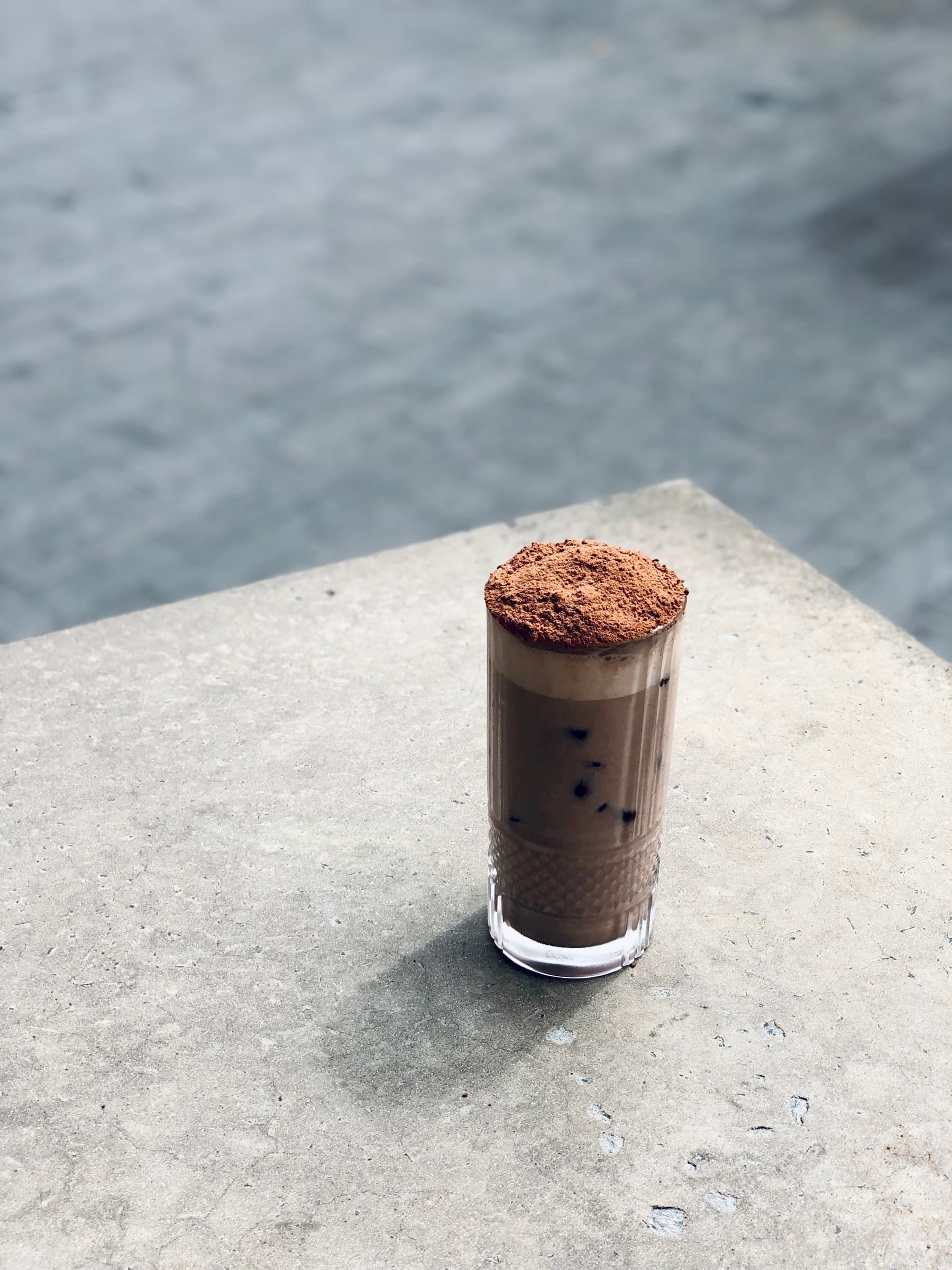 Iced mocha topped with cocoa powder, on a polished concrete bench