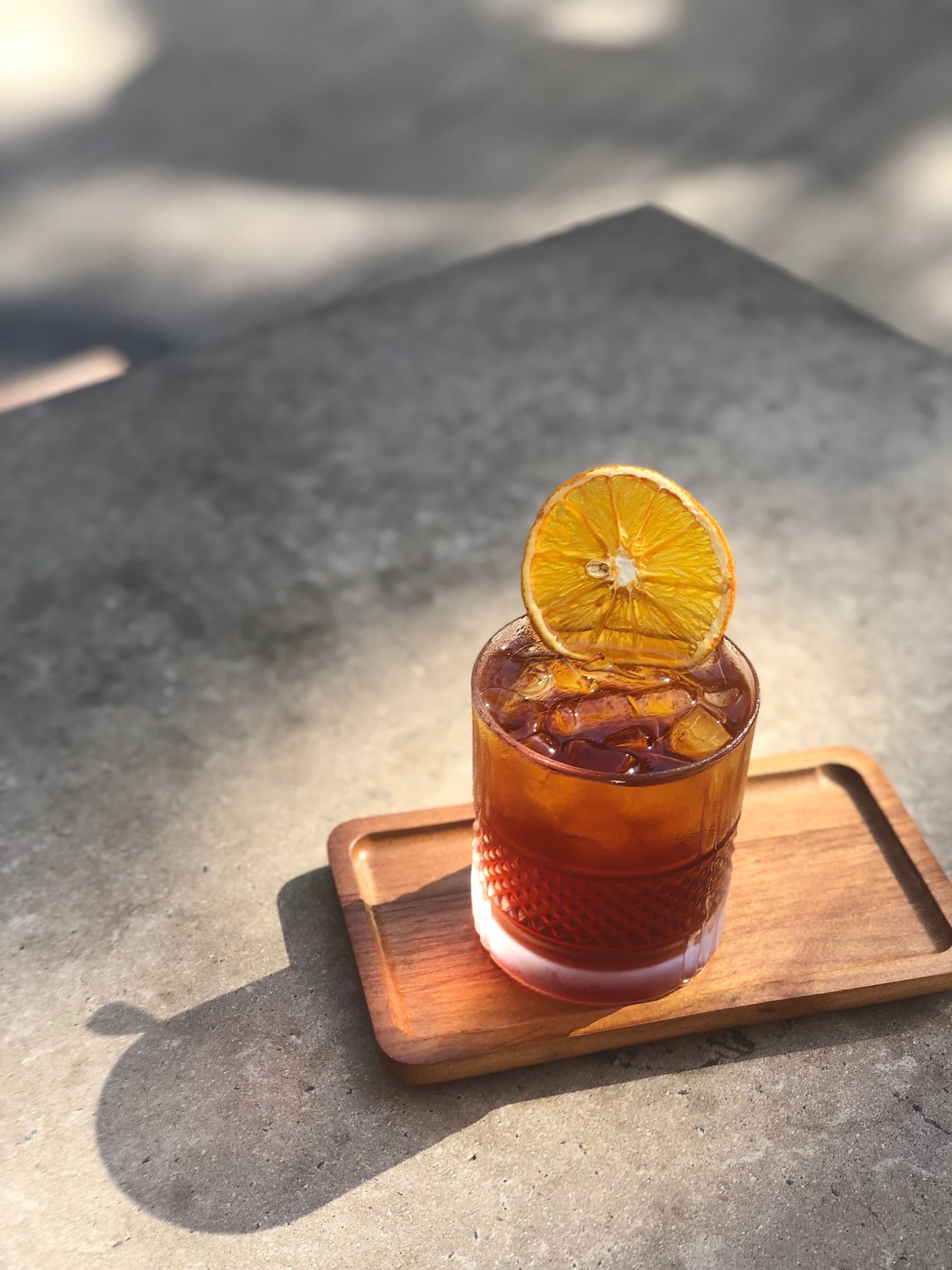 A Negroni in a cut-glass rocks tumbler with a dried orange slice, late-afternoon shadow on concrete