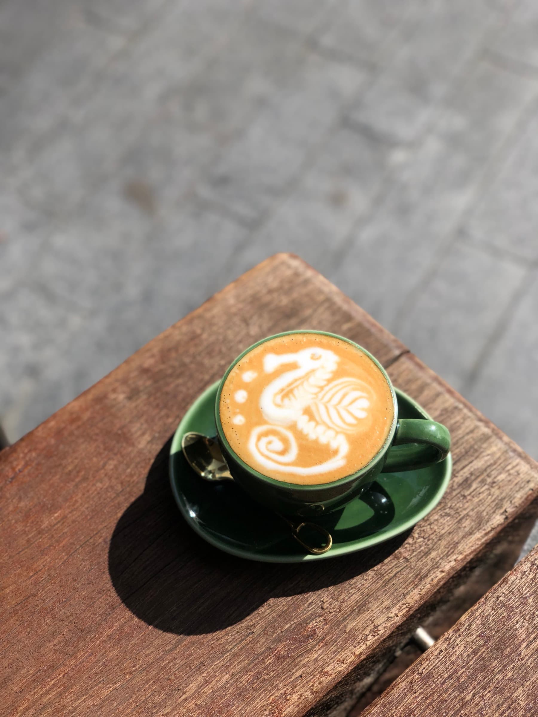 Five Senses single-origin latte with a seahorse poured, on a green ceramic saucer